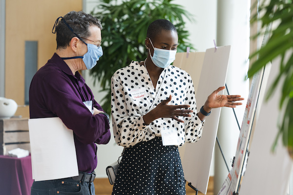 A faculty member listens to a graduate student explain her research poster.